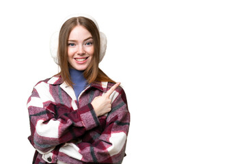 Sticker - Young pretty woman wearing winter muffs over isolated chroma key background pointing to the side to present a product