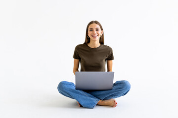Portrait of a smiling casual woman holding laptop computer while sitting on a floor isolated over white background