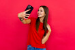 Handsome young woman is taking a selfie on phone over red background.