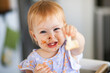 © Austockphoto - One year old baby with messy face holding out piece of toast to share