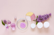 Development Of New Types Of Natural Cosmetics With Floral Extract And Lilac Aroma. Moisturizing Face Cream In White Jars, Facial Wash In Petri Dish And Lilac On Laboratory Table. Flat Lay, Copy Space