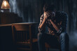 Depressed man sitting on the chair and holding his forehead while having headache in the dark bedroom with low ligh