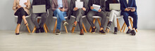 Legs Of Unrecognizable Business People Sitting On The Chairs In A Row With Resumes And Laptops In Their Hands. Group Of A Staff. Job Candidates Seekers Waiting For Interview Invitation Turn. Banner.