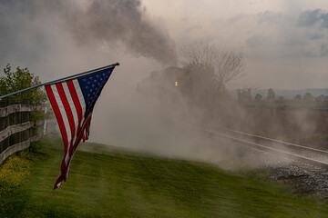 Sticker - A Steam Locomotive Backing Up Blowing Lots of Smoke With a America Flag Waving on a Fence