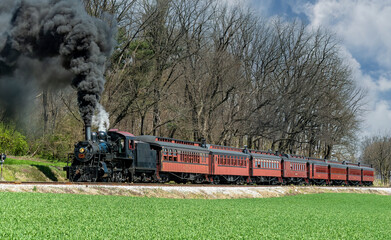 Canvas Print - An Angled View of a Restored Steam Passenger Train Moving Slowly Blowing Lots of Black Smoke and White Steam on a Sunny Day