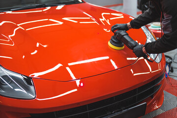 Car detailing concept. Worker with orbital polisher working on a red sports car in auto repair shop. High quality photo