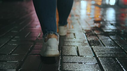 Wall Mural - legs of a girl walking in front of the camera on a wet sidewalk, rear view