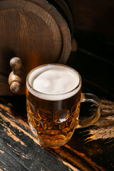 Mug of cold beer and oak barrel on dark wooden background