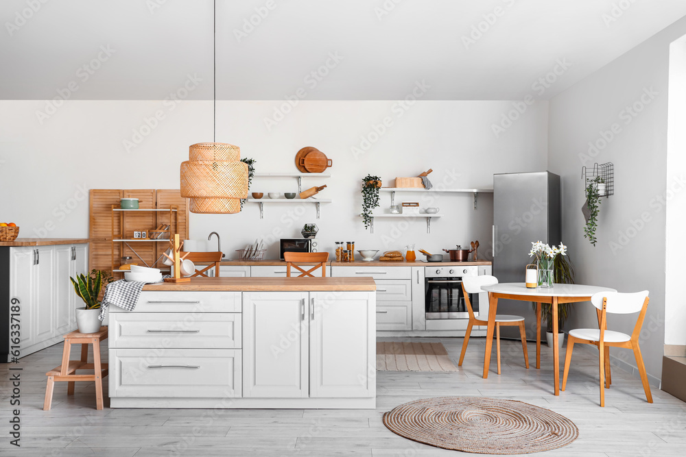 Interior of light kitchen with stylish fridge, counters, shelves and table