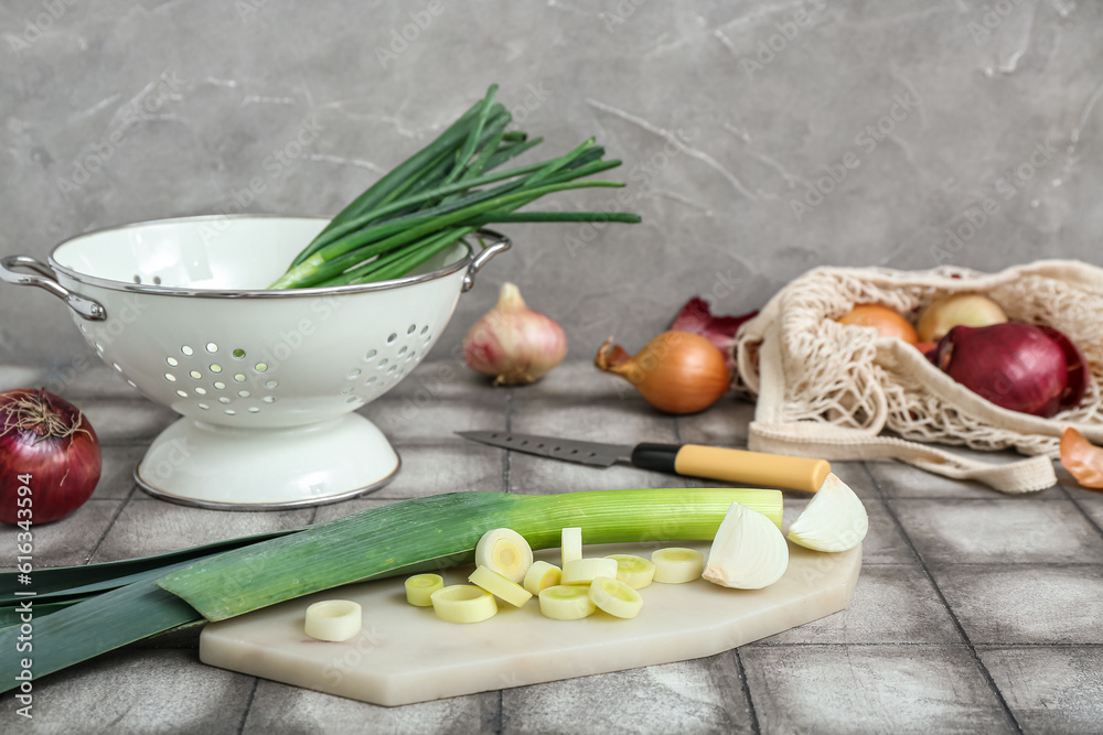 Board, colander and string bag with different kinds of onion on grunge grey table
