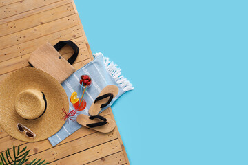 Different beach accessories with bowl of strawberry, cocktail and plant branches on wooden pontoon against blue background. Summer vacation concept