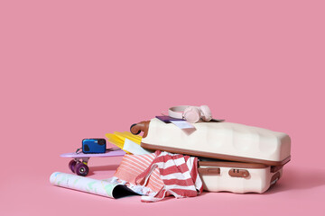 Sticker - Suitcase with passport, headphones, map and beach accessories on pink background. Travel concept