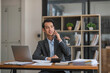 © chartchai - Portrait of a professional Asian businessman looking some details on a paper while talking on the phone with his supplier in the office.