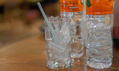 Ice cubes in an empty glass with straw and water bottles on a wooden bar counter in the restaurant.