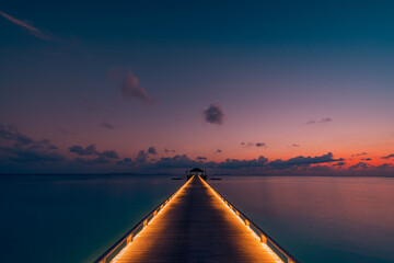 Wall Mural - Amazing sunset panoramic beach Maldives. Luxury resort villas long wooden pier seascape with soft led lights under colorful sky view with calm sea and relaxing tropical mood. Amazing travel landscape