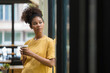 © Songsak C - A smiling black woman drinking coffee while standing near a window at a cafe, a Happy young African American female holding a cup with a hot drink and looking away.