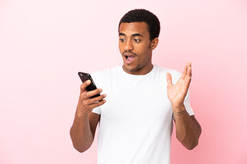 Poster - African American handsome man on isolated pink background looking at the camera while using the mobile with surprised expression