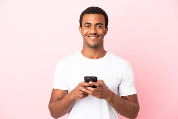 Canvas Print - African American handsome man on isolated pink background looking at the camera and smiling while using the mobile