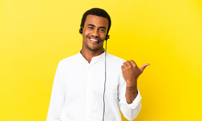 Wall Mural - African American Telemarketer man working with a headset over isolated yellow background pointing to the side to present a product