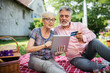 © Mediteraneo - Elderly couple buying online with their card.Sitting in the backyard while having a picnic.