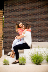 Smiling young couple in love sitting in front of house brick wall