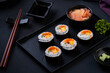 Maki sushi on black tray.Japanese sushi rolls with salmon, cucumber, shrimp eggs and Imitation Crab Stick with soy sauce dip and chopsticks on black table background.