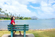 Young woman resting on park bench enjoying the sunshine along Hawaiian ocean