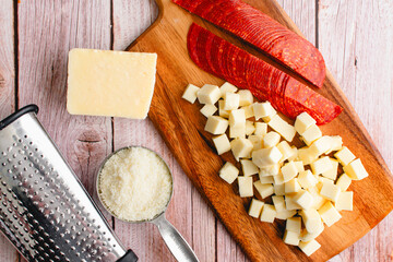 Wall Mural - Prepped Pepperoni, Mozzarella, and Parmesan Cheese on a Wooden Background: Sliced pepperoni with chopped and grated cheese and a box grater