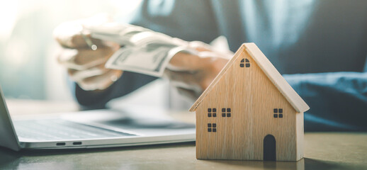 Wall Mural - Businessman choosing mini wood house model from model and row of coin money on wood table, selective focus, Planning to buy property. Choose what's the best. 