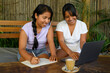 © Franci Leoncio - Cheerful latin young women taking notes while working on laptop in cafe