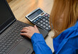Kobieta przy biurku używająca kalkulatora i laptopa 