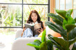 © freebird7977 - Happy young woman reading book on sofa at home.  Lifestyle freelance relax and chill drinking coffee in living room, Nature garden background.  Lifestyle Concept
