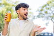 Young Arabian handsome man holding an orange juice at outdoors with surprise facial expression