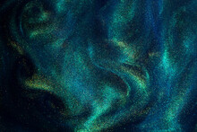 Various Stains And Overflows Of Gold Particles In Blue Fluid With Green Tints. Golden Particles Dust And Smooth Defocused Background. Liquid Iridescent Shiny Backdrop With Depth Of Field.