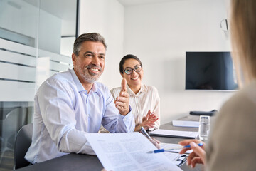 Smiling Latin manager working with diverse colleagues at team meeting. Happy diverse business people international corporate executives talking at group briefing, collaborating at boardroom table.