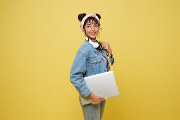 Happy Asian girl student with laptop and backpack isolated on yellow studio background.