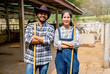Portrait of Asian man and woman farmers carry broom and stand with arm crossed also look at camera with smiling in front of stable of cow look relax after clean the area.