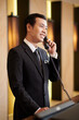 © DragonImages - Luxurious hotel receptionist in elegant suit answering phone call