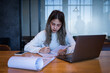 © EduLife Photos - A serious college student studies in a library, looking at her laptop and writing in a notebook