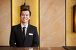 © DragonImages - Portrait of positive Asian hotel receptionist with badge on his suit
