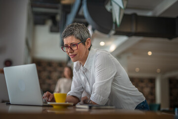 One senior business woman working on laptop in the cafe and drinking coffee from yellow cup, modern business and lifestyle concept