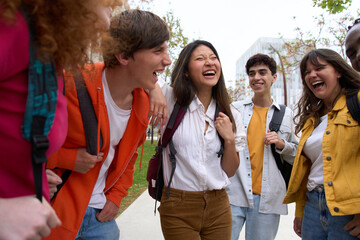 Wall Mural - Diverse group of smiling young students gathered outside college campus. Happy classmates and friends enjoying the break between classes. Generation z people laughing outdoors together on spring day.