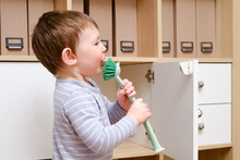 Happy Toddler Baby With A Cleaning Brush In The House. A Funny Child Is Holding A Large Brush In His Hands.