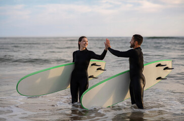 Wall Mural - Happy Man And Woman In Wetsuits Giving High Five After Surfing Together