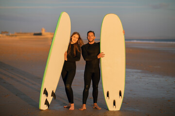 Wall Mural - Happy Young Couple Posing With Their Surfboards On The Beach At Sunset