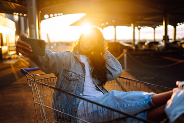 Wall Mural - Selfie time. Young woman having fun on shopping trolleys. Black friday. Consumerism, sale, discounts, lifestyle concept.