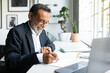 © Prostock-studio - Cheerful mature european man in suit work on laptop, making notes, signing contract in modern office
