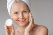 © Prostock-studio - Aged skincare routine. Happy aged woman applying moisturizing cream on face, showing jar with nourishing lotion, closeup