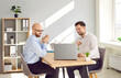© Studio Romantic - Business men at work in office. Two young smiling employers sitting at the desk on meeting looking at laptop monitor screen and smiling discussing new projects or startups, analyzing company.