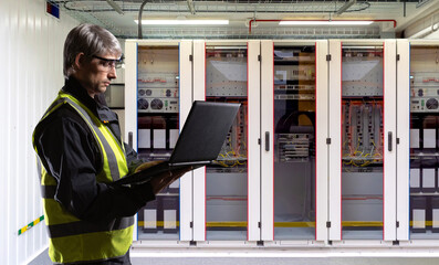 Poster - Man technician with laptop. Manufacturing plant engineer. Technician controls electrical equipment. Cabinets with equipment for factory automation. Man technician uses computer. Factory worker